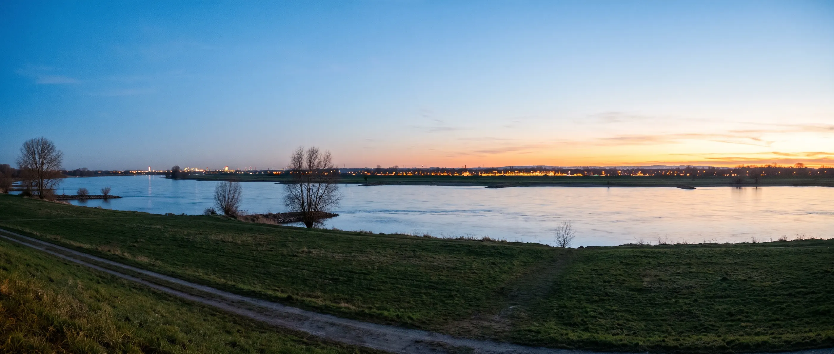 Rheinufer am Abend mit fernen Lichtern am anderen Ufer (Stimmungsbild)